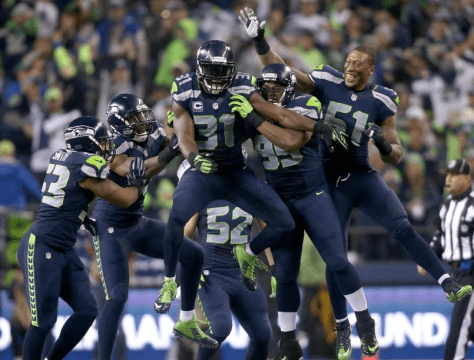 Teammates mob Kam Chancellor (31) after his stunningly stellar stunt on a field goal attempt seemed to succeed vs. Carolina (Seahawks.com)